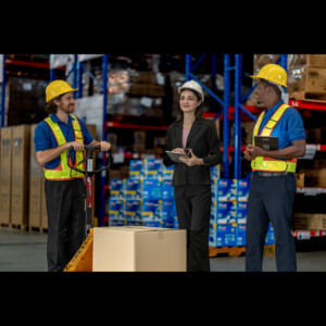Co-workers in hard hats gathered in a warehouse discussing business